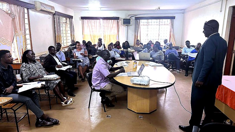 Academic staff attending a CBET workshop at Kyambogo University's IICD Conference Room, with a facilitator presenting to a full room of participants seated around tables.